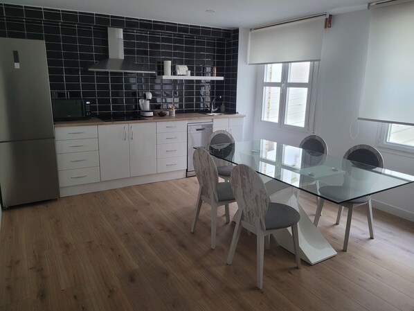 A modern kitchen with black tiled backsplash, white cabinets, and a glass dining table with four chairs.