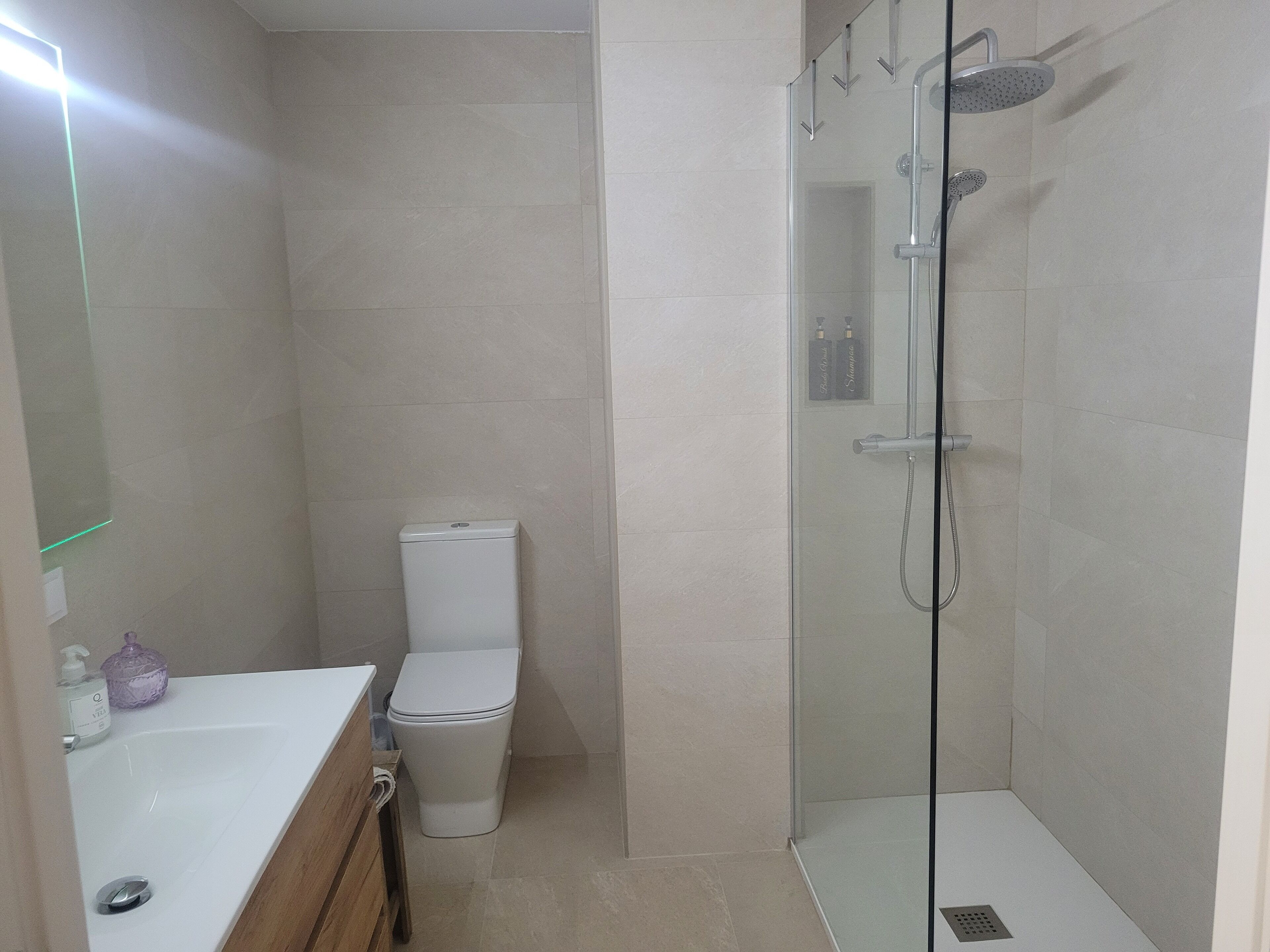 A bathroom with a toilet, a glass-enclosed shower, and a sink with a mirror.
