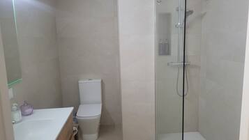 A bathroom with a toilet, a glass-enclosed shower, and a sink with a mirror.
