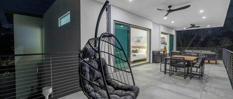 A modern outdoor patio with a hanging chair, a dining table with chairs, and a ceiling fan.