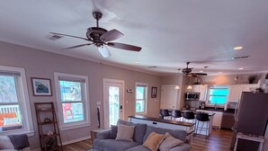 A modern living room with a grey sofa, ottoman, and a ceiling fan. - Bolivar Beachside Getaway (Crystal Beach)