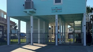 A light blue building with a covered entrance, a sign reading 'Coastal Houglass,' and a gated driveway. - Bolivar Beachside Getaway (Crystal Beach)