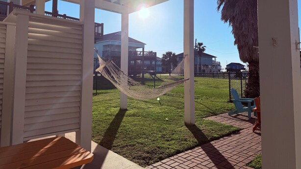 A covered outdoor area with a hammock, a wooden bench, and a view of houses in the background. - Bolivar Beachside Getaway (Crystal Beach)