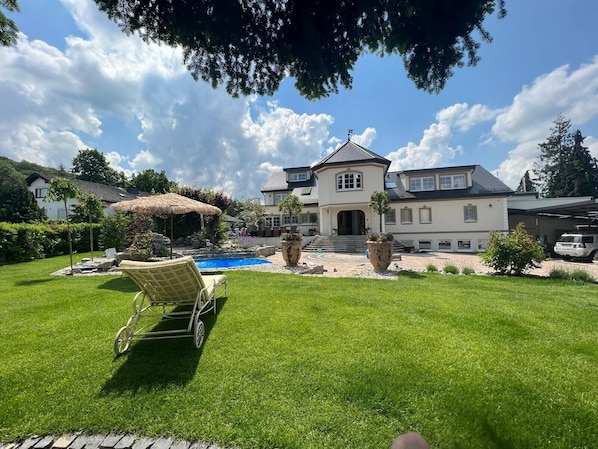 A large house with a swimming pool, a lawn, and a patio area.