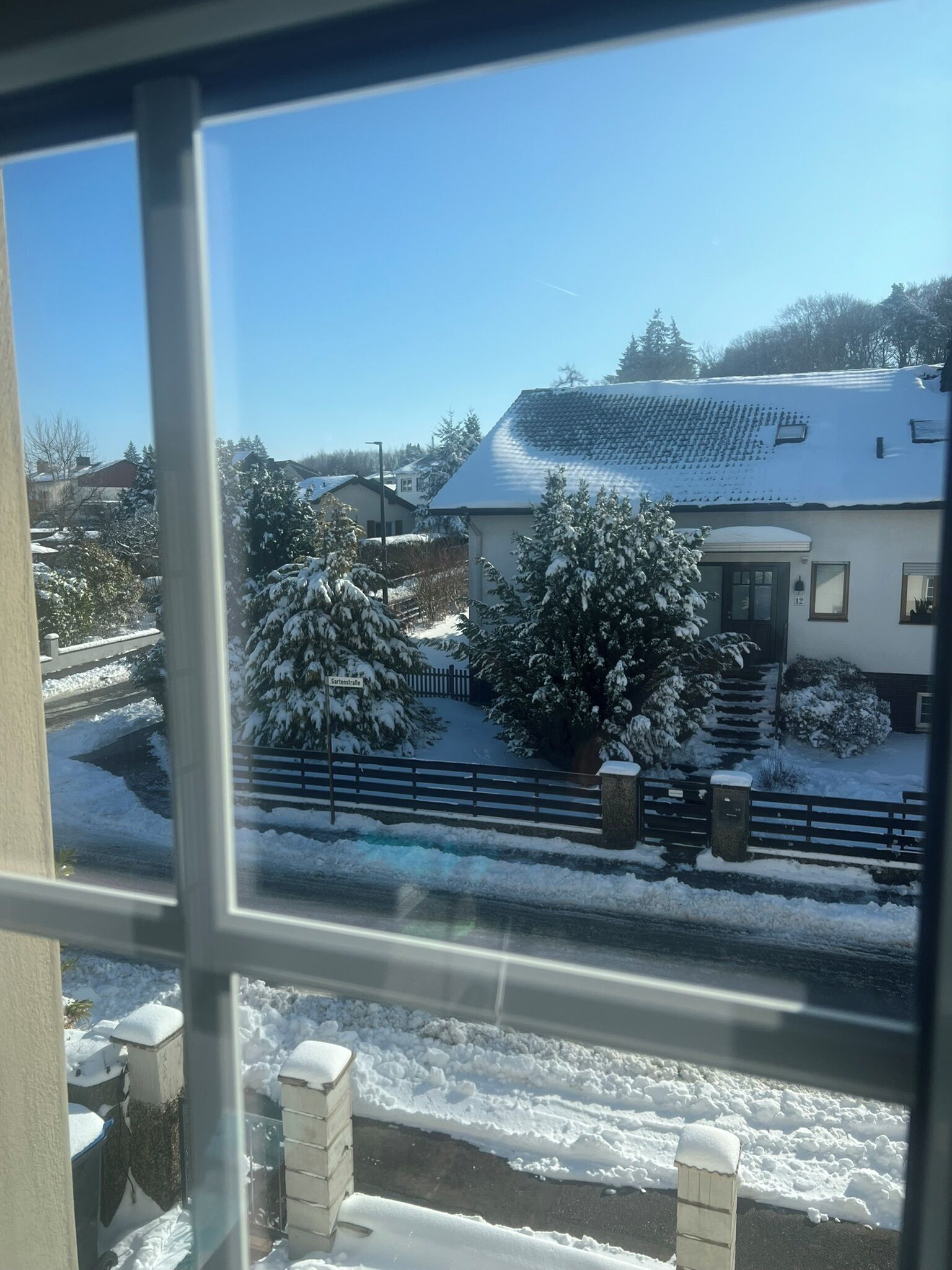 A residential area with snow-covered houses, a clear sky, and a street visible through a window.