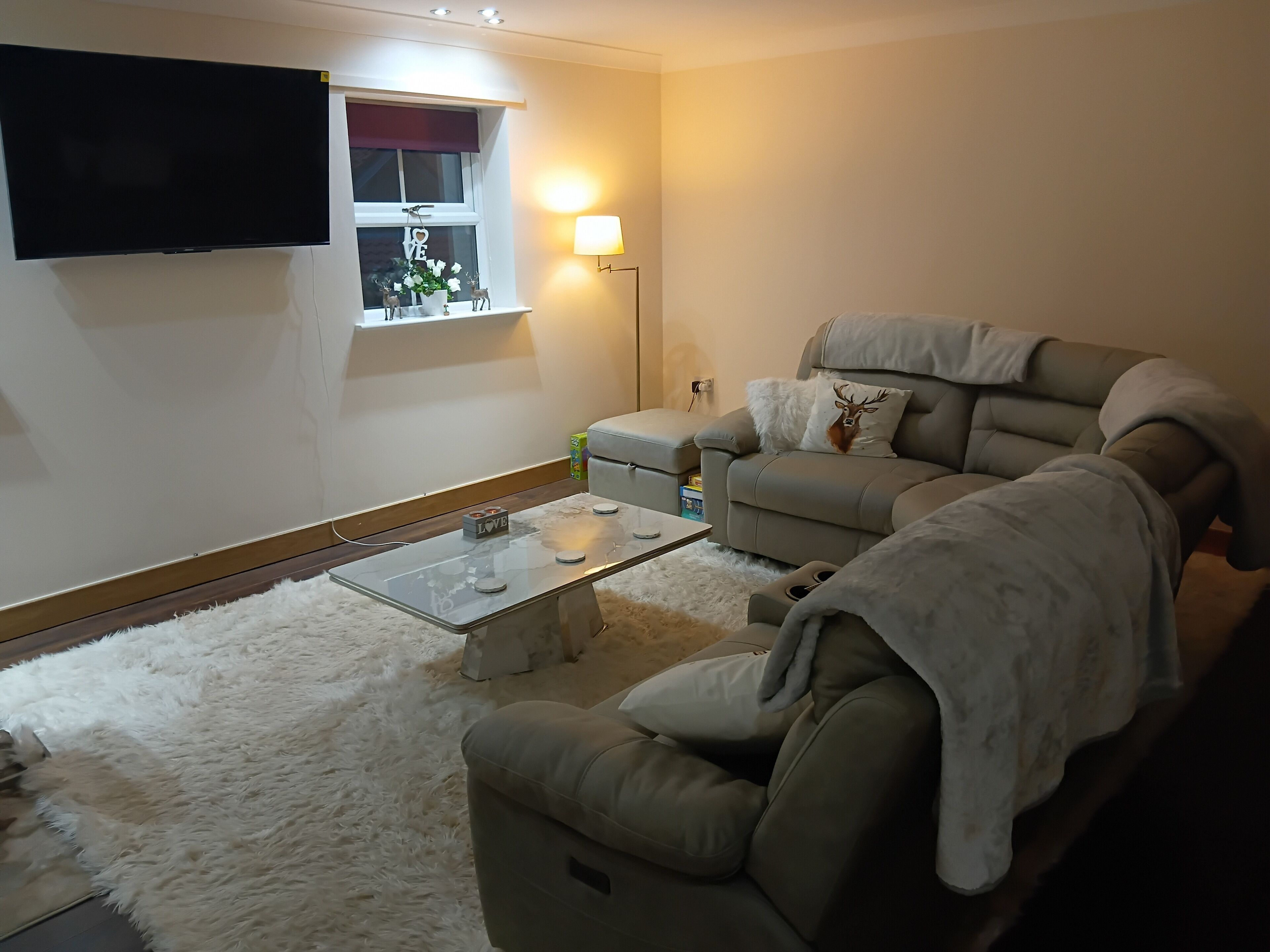 A living room with a sofa, a coffee table, a TV, and a window with a decorative item.