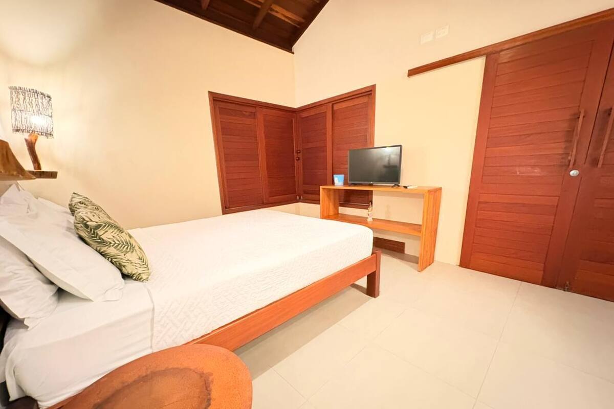A bedroom with a bed, a TV on a wooden stand, and two wooden wardrobes.