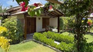 A house with a covered porch, a well-maintained lawn, and various flowering plants. - Pousada Rancho Paraiso (Porto de Pedras)