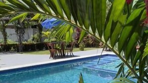 A clear blue pool surrounded by lush greenery and a red flower. - Pousada Rancho Paraiso (Porto de Pedras)