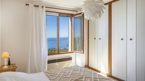 Ein Schlafzimmer mit großem Fenster, einem Bett, einem Nachttisch mit Lampe und einem Kleiderschrank.