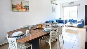 Een eetruimte met een houten tafel, witte stoelen en een schilderij van een stadsgezicht aan de muur.