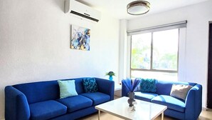 Een woonkamer met twee blauwe banken, een witte salontafel en een groot raam met uitzicht op groen.