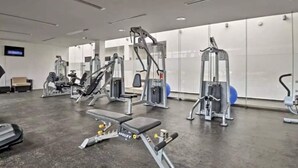 Een sportschool met diverse fitnessapparaten, een bank en een televisiescherm aan de muur.