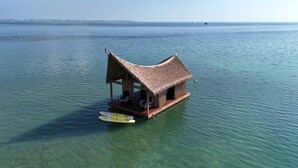 A floating structure with a thatched roof, seating area, and a surfboard. - The Grand Tiki at Tiki Suites – A Floating Oasis in Key West (Key West)