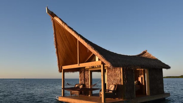 A floating wooden structure with a thatched roof, a hammock, and a small seating area, situated on calm water. - The Grand Tiki at Tiki Suites – A Floating Oasis in Key West (Key West)