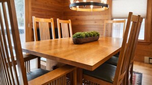 Une table à manger en bois, accompagnée de six chaises, un lustre moderne et une petite plante en pot.