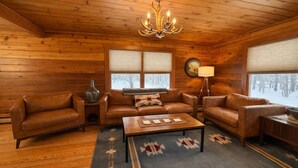 L’intérieur d’un chalet confortable, avec des canapés en cuir, une table basse en bois et un lustre.