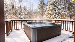 Un bain à remous sur une terrasse en bois, entouré d’arbres couverts de neige.