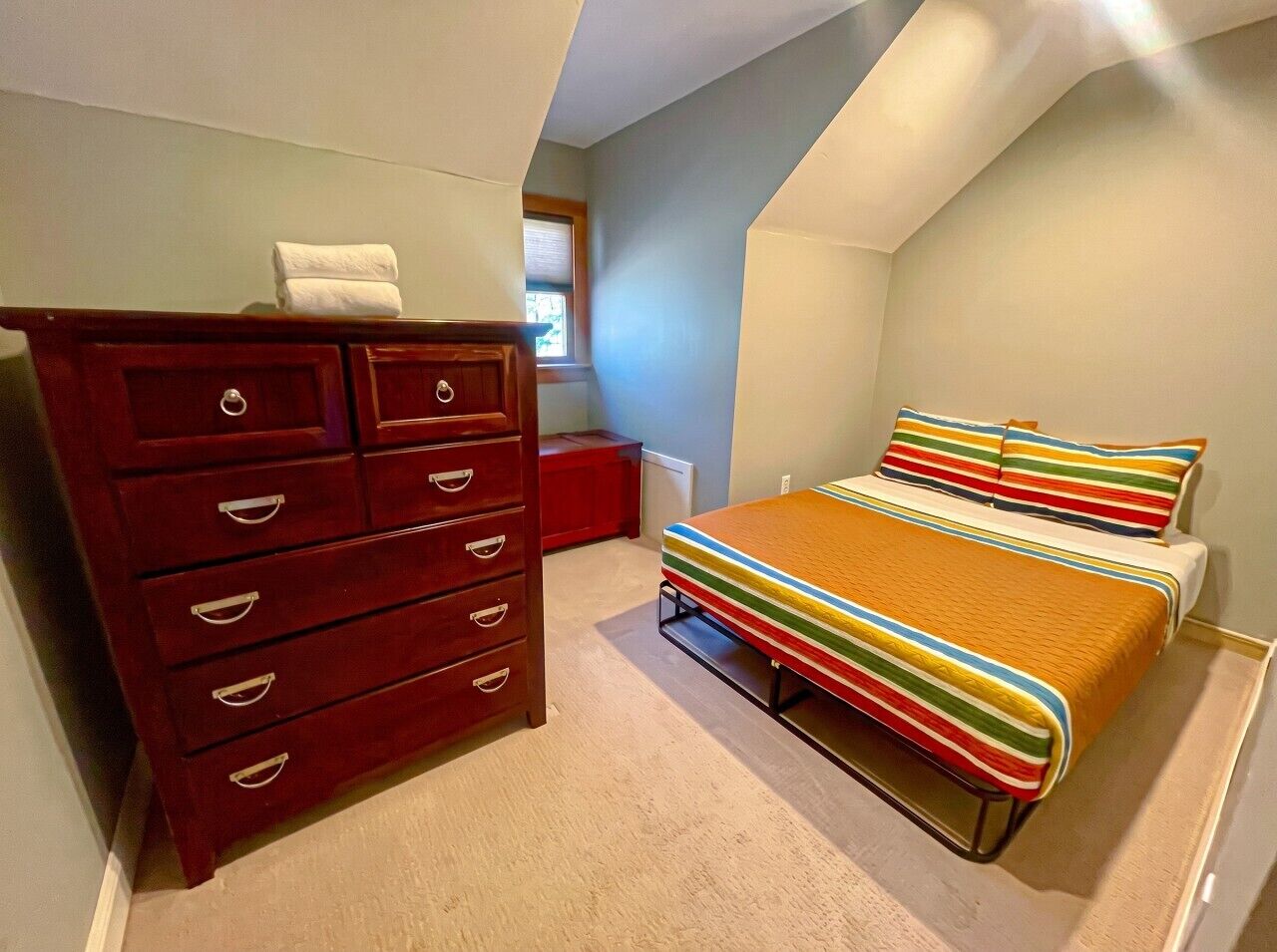 Un dormitorio con cama, cómoda y ventana.
