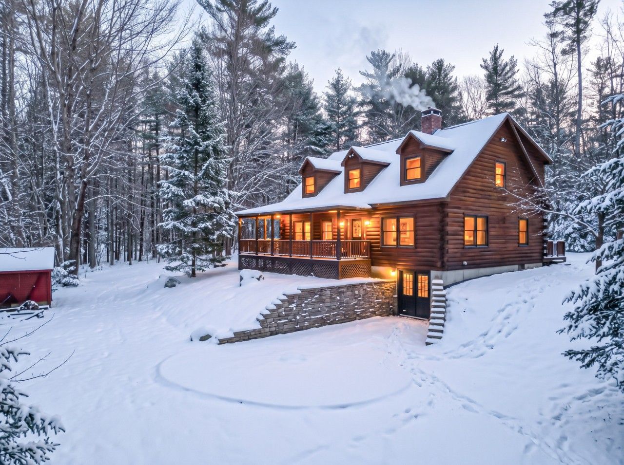 A wooden cabin with a covered porch, surrounded by snow-covered trees.