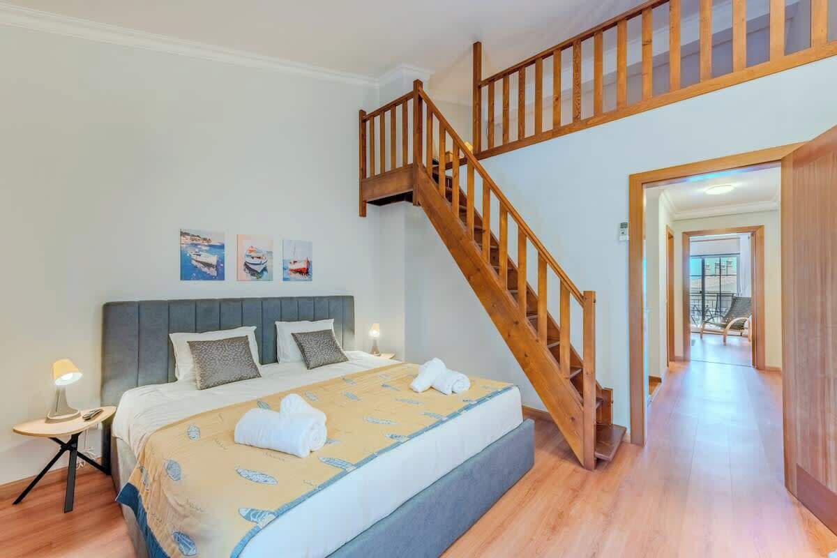 Une chambre à coucher avec un lit, une table de chevet, un escalier en bois et une vue sur un balcon.