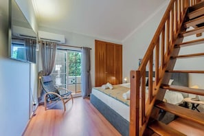 A bedroom with a wooden staircase, a bed with a blue headboard, a window with curtains, and an air conditioning unit. - Sao Rafael villa Rosal with pool (Albufeira)