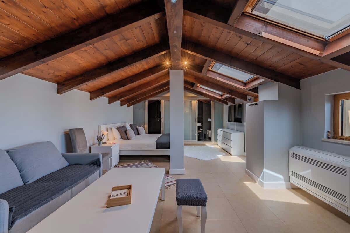 Amplia habitación en ático con techo alto, vigas de madera, un sofá, una mesita y un radiador.