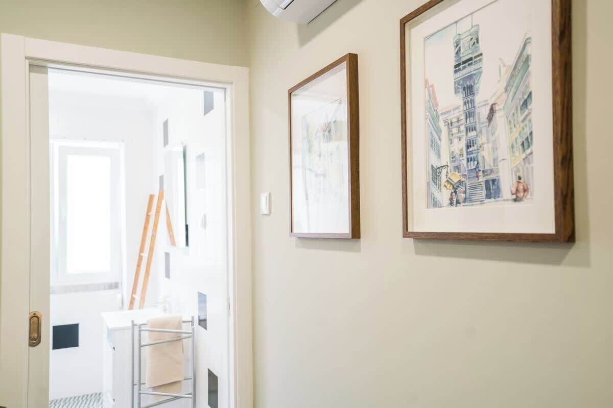 A hallway with a door leading to a room, a ladder, and two framed artworks on the wall.