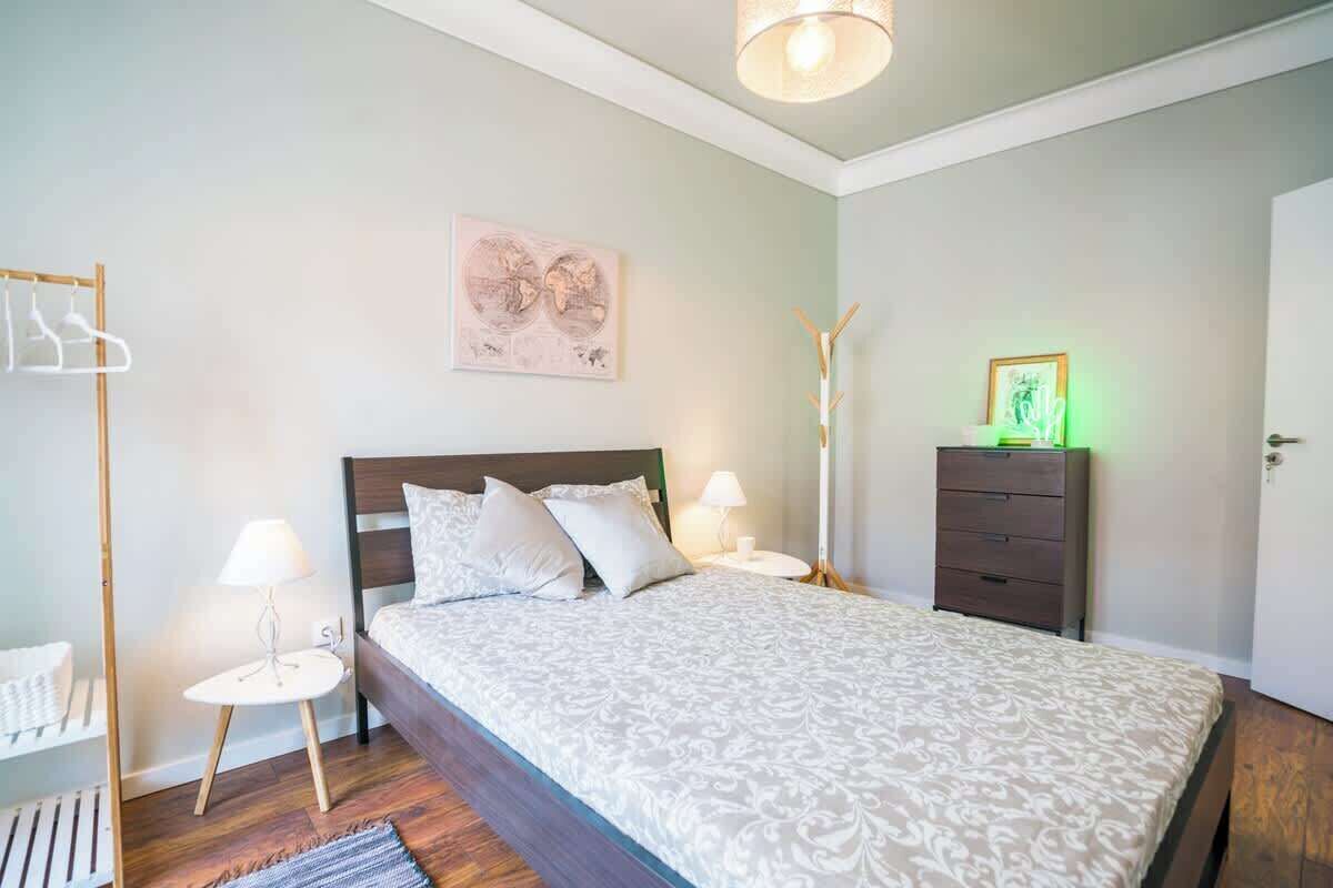 Une chambre à coucher bien rangée, avec un lit, des tables de chevet, une commode et une œuvre d’art accrochée au mur.