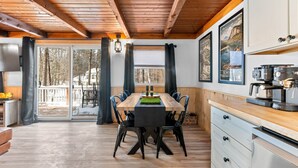 Une cuisine moderne avec des poutres en bois, un coin repas doté d  ’une longue table et une vue sur une terrasse enneigée.