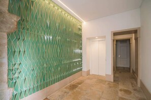 Ein Flur mit grüner geometrischer Wand, einer weißen Tür und Steinböden.