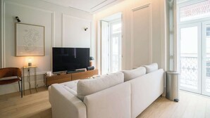 Ein modernes Wohnzimmer mit einem großen Flachbildfernseher, einem weißen Sofa und einem kleinen Tisch mit einer Lampe.