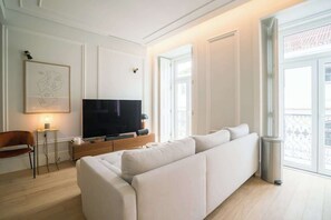 Ein modernes Wohnzimmer mit einem großen Flachbildfernseher, einem weißen Sofa und einem kleinen Tisch mit einer Lampe.