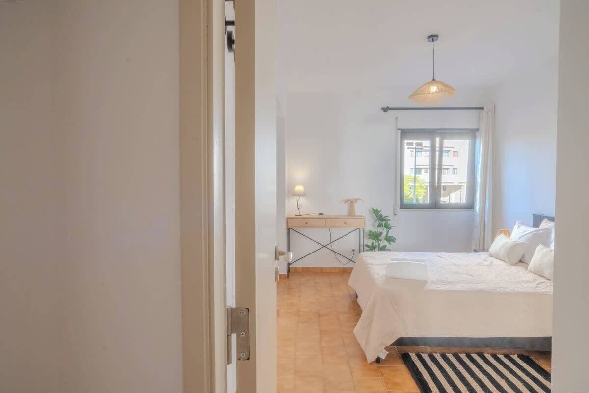 A bedroom with a bed, a desk, a lamp, and a window.