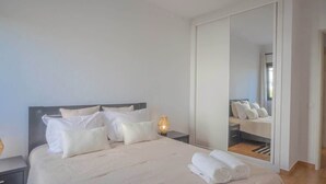 A neatly made bed with white linens and pillows, a bedside lamp, and a large mirror reflecting the room. - Casa Rocha Portimao with Terrace (Portimão)