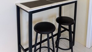A small, square table with a black metal frame and a white marble-like top. There are two black stools with round seats. A power outlet is visible on the wall to the left. - Central & Secure Stay - Minutes from Town, Airport and Stadium (Osbourn)