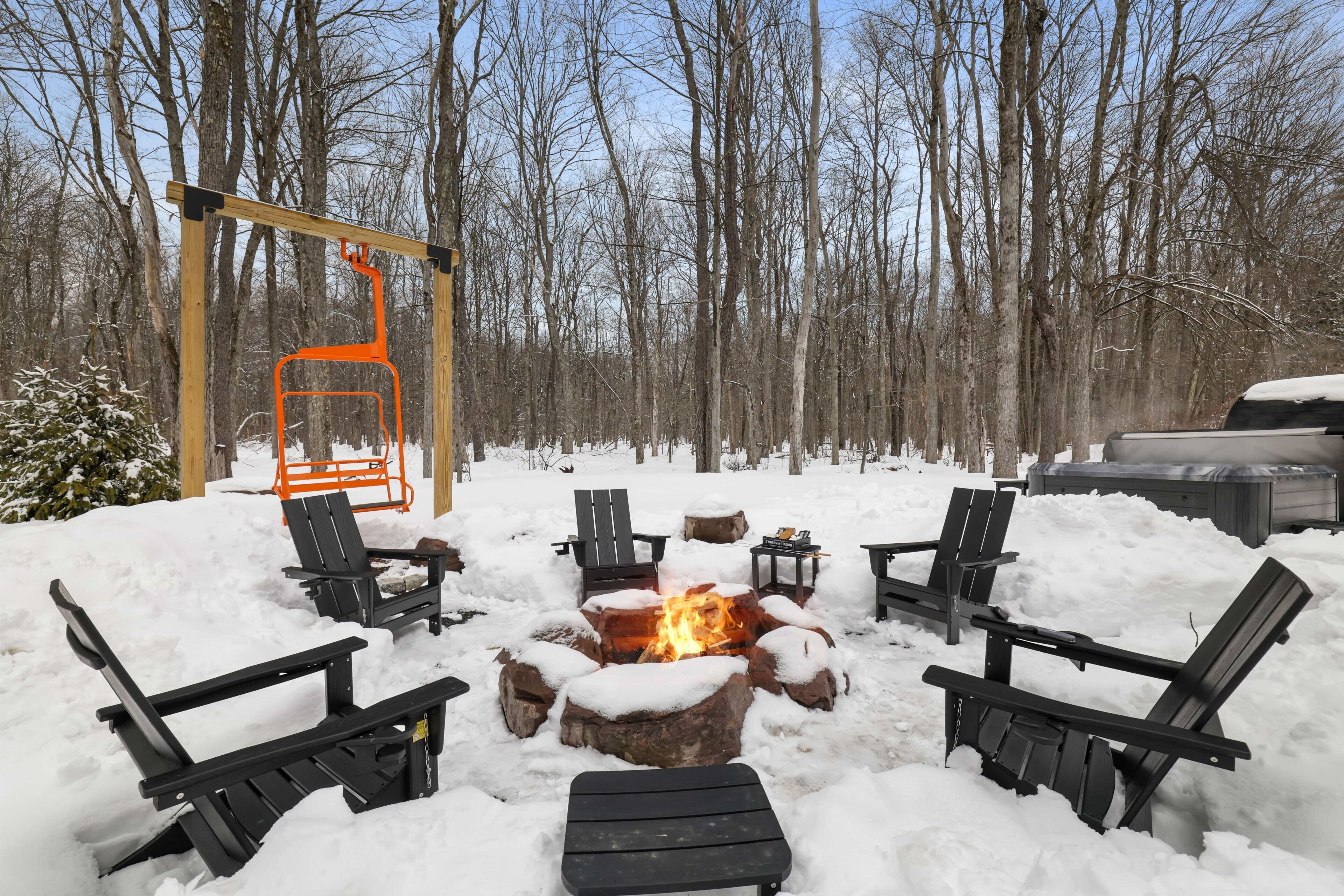 Un espace extérieur aménagé avec des sièges, recouvert de neige, comprenant des fauteuils Adirondack et un foyer.