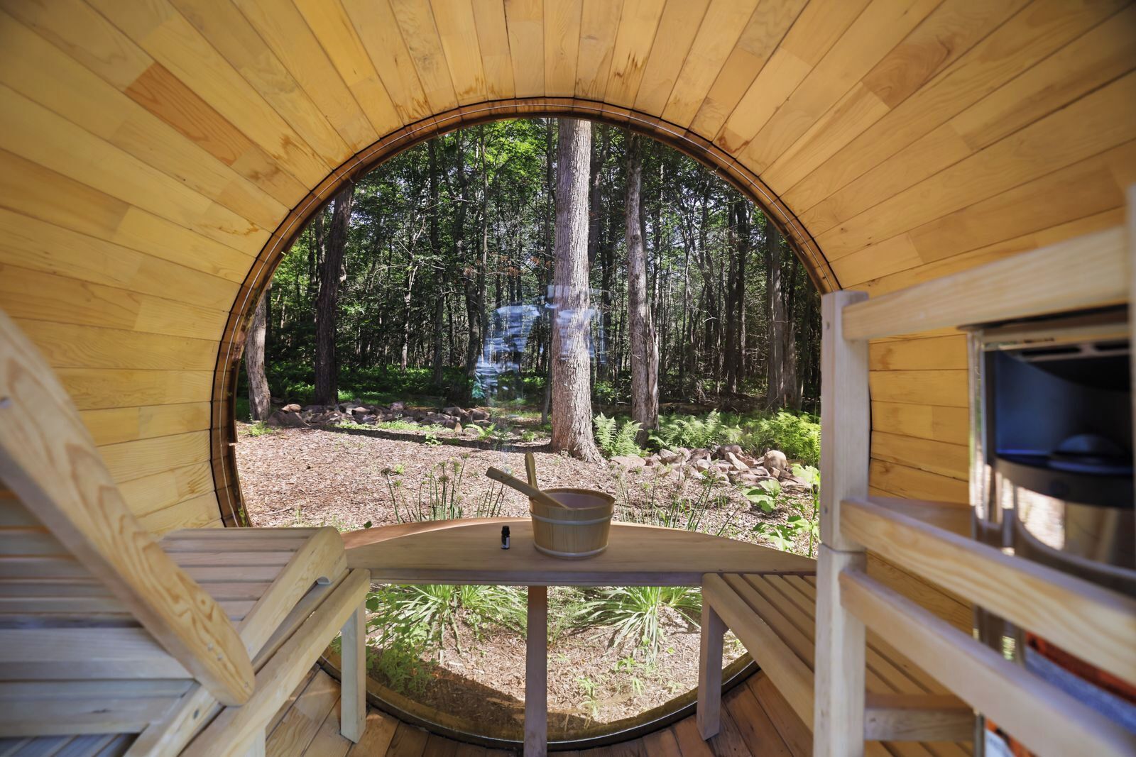 Il s’agit d’une structure circulaire en bois, d’où l’on peut admirer une forêt. À l’intérieur, on trouve une table, un seau et une bouteille.
