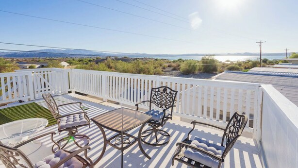 Un balcón con mobiliario exterior, una cerca blanca y vistas a un paisaje montañoso.