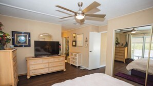 Un dormitorio con cama, cómoda, televisor y ventilador de techo.