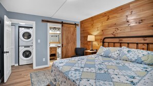 Una camera da letto con un letto, una testiera in legno, un comodino, una lampada, una sedia e un angolo lavanderia con lavatrice.