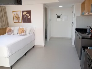 Quarto de hotel moderno com uma cama, uma kitchenette e um corredor que dá para outro quarto.