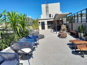 Un'area patio all'aperto con posti a sedere, piante in vaso e un edificio moderno sullo sfondo.