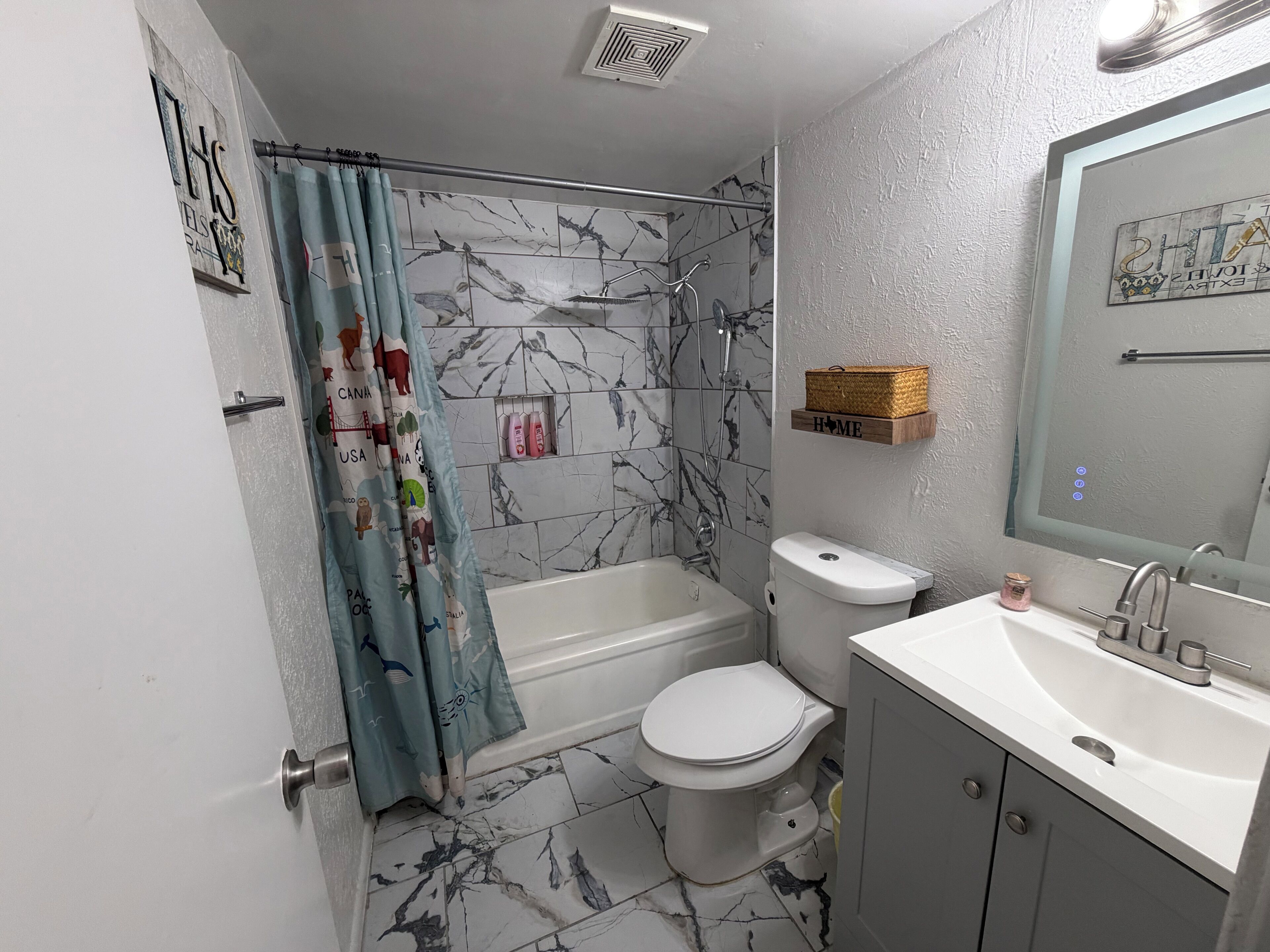 A bathroom with a shower, toilet, and sink, marble-patterned walls, and a shower curtain with animal prints.