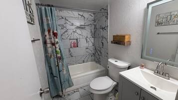 A bathroom with a shower, toilet, and sink, marble-patterned walls, and a shower curtain with animal prints.