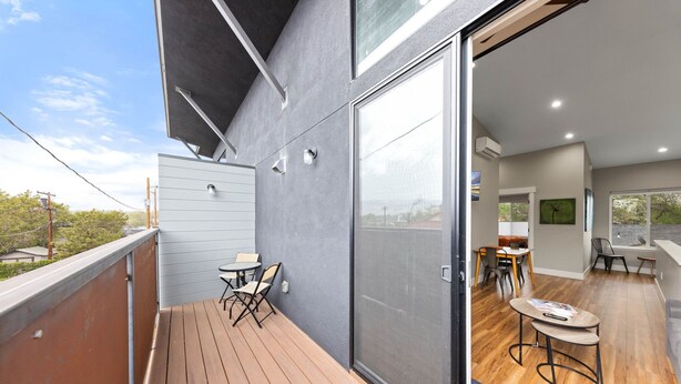 A balcony with a wooden deck, a sliding glass door leading to an interior dining area with a table and chairs, and a view of the outdoors. - Modern Midtown Oasis: Mountain Views & Walkable Vibes (Reno)