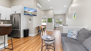 A modern kitchen with a stainless steel refrigerator, a dining area with a table and chairs, a gray sofa with a patterned pillow, and a small round table with a remote control. - Modern Midtown Oasis: Mountain Views & Walkable Vibes (Reno)