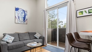 A living room with a grey sofa, a small round table, a pair of brown chairs, a sliding glass door, and a framed picture on the wall. - Modern Midtown Oasis: Mountain Views & Walkable Vibes (Reno)