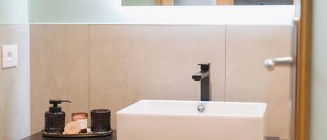 A bathroom with a white sink, a mirror above it, and a black shelf below. There are two woven baskets on the shelf.