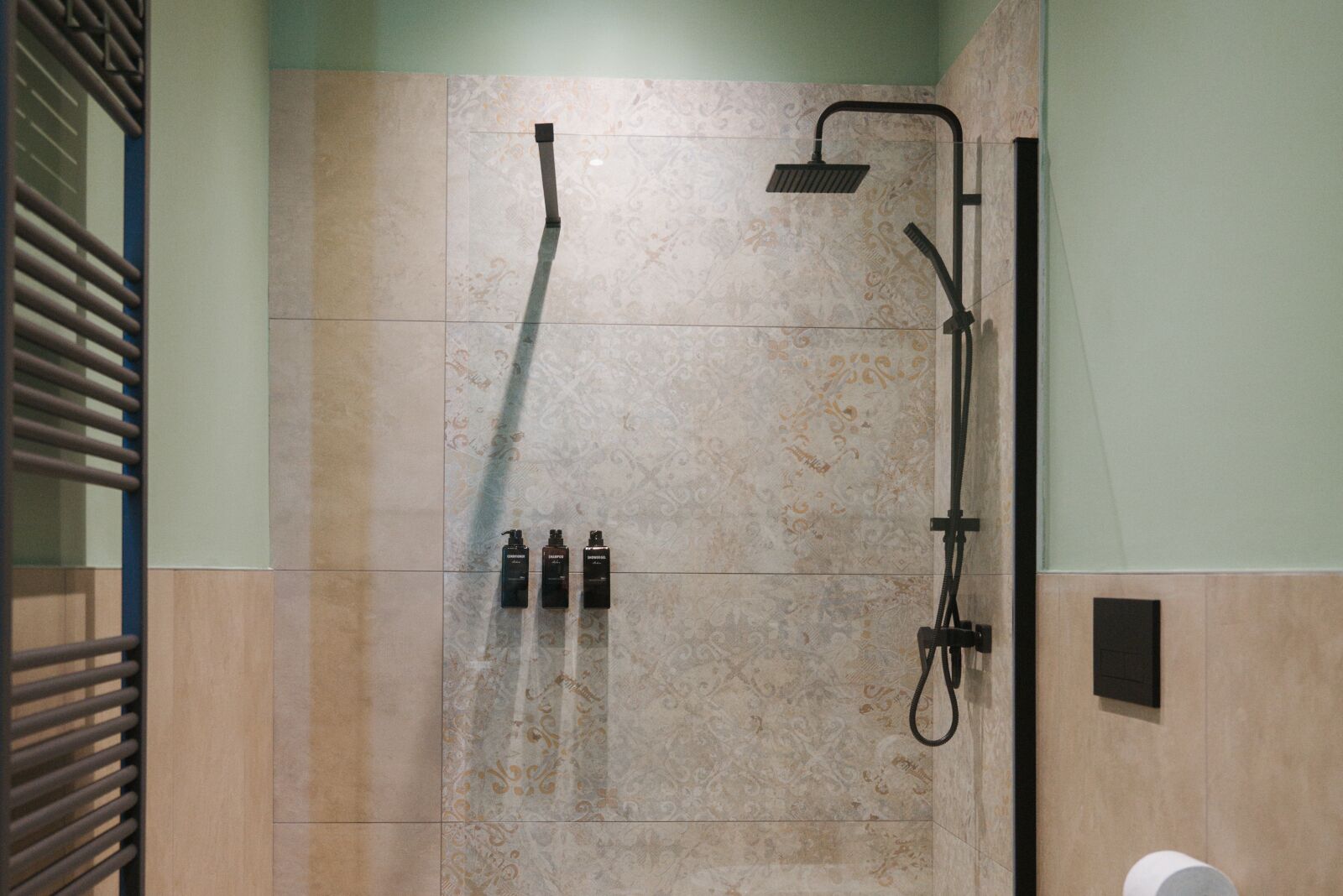 A shower area with a rain showerhead, handheld showerhead, and three bottles of shampoo.